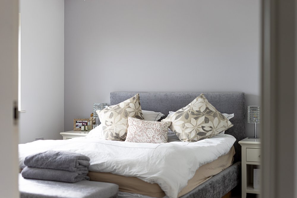 Bedroom reveal shot framed through an open doorway, foreground softly out of focus with the bed as the sharp focal point