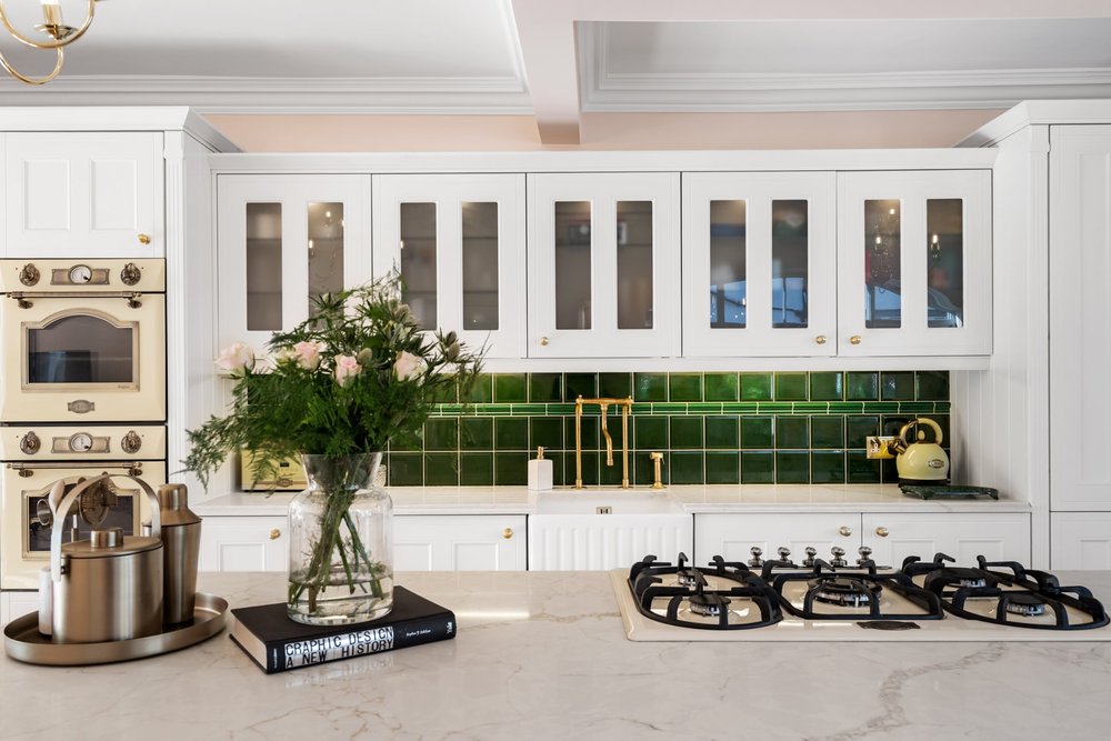 Detail shot of a white shaker kitchen with green tiled splashback, brass tap and a styled marble island